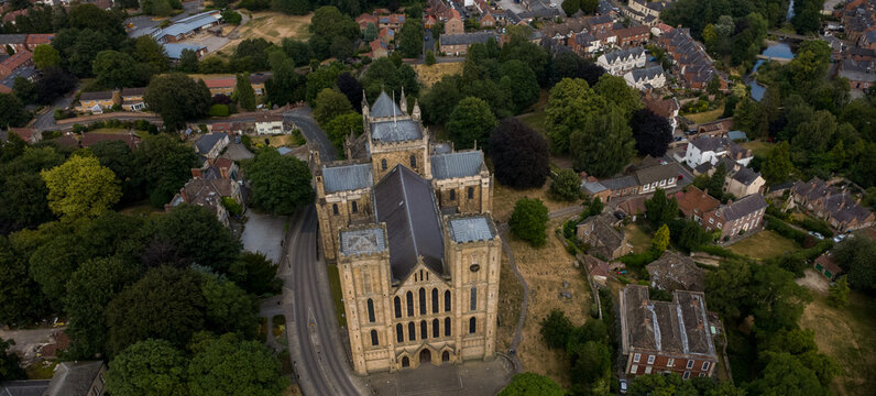 Aerial view of Ripon Cathedral surrounded by lush green trees, historic stone architecture, and residential rooftops in Ripon, England, United Kingdom.