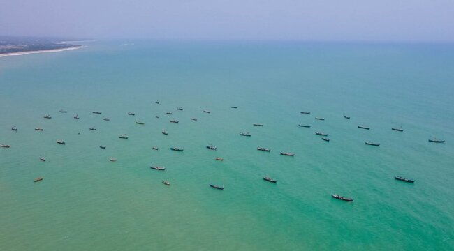 Aerial view of numerous small wooden fishing boats scattered across the turquoise waters of the Atlantic Ocean off the coast of Ghana.