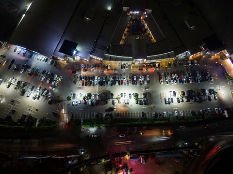 Aerial view of a busy parking lot at night illuminated by bright artificial lights with rows of parked cars and surrounding commercial buildings in Ghana.