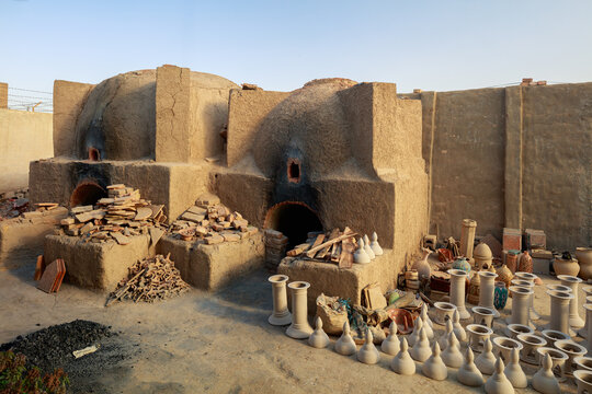 View of traditional mud-brick kilns used for firing pottery, surrounded by numerous unglazed clay vessels and ceramic objects in a workshop setting in Hala, Sindh, Pakistan.
