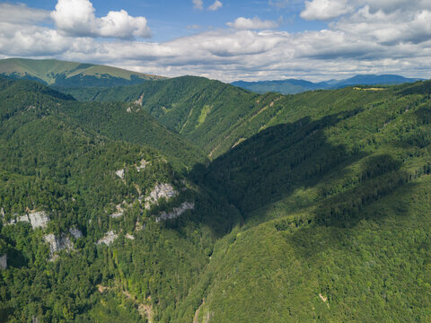 Aerial view of Bystricka dolina in the Velka Fatra mountains, featuring lush green forested slopes, rocky outcrops, and shadows cast by clouds in Dolny Harmanec, Banskobystricky kraj, Slovakia.