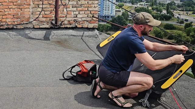 Man Setting Up Portable Foldable Solar Panel on a Rooftop for Alternative Energy