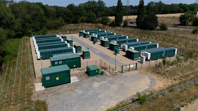 Aerial view of a modern industrial battery energy storage facility with rows of green containers and electrical infrastructure surrounded by trees in Hatfield, England, United Kingdom.