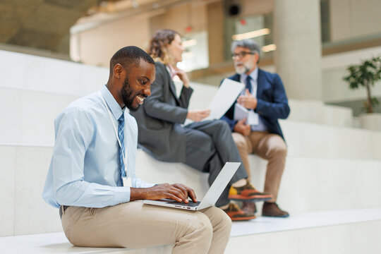 Smiling young businessman using laptop while sitting on steps in office