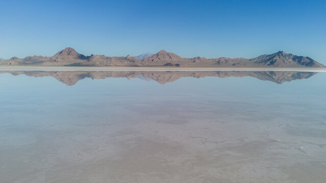 Aerial view of the expansive Bonneville Salt Flats with mountains reflected in the thin layer of water under a clear blue sky in Tooele County, Utah, United States.