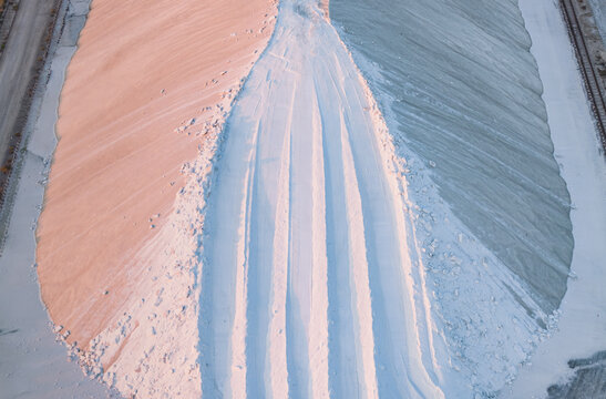 Aerial view of contrasting sea salt stockpiles divided by a sculpted central haul road with parallel vehicle tracks in France.