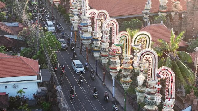 Aerial view of Pura Agung Petilan decorated with traditional Balinese penjor along the street with traffic in Kecamatan Denpasar Timur, Bali, Indonesia.