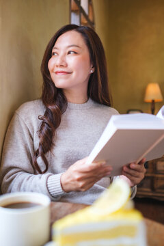 Vertical portrait image of a woman reading a book with coffee cup and a lemon cake on the table