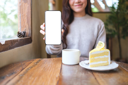 Mockup image of a woman holding and showing a mobile phone with blank white screen in cafe