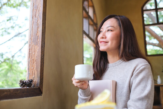 Portrait image of a woman holding a book and drinking coffee in cafe