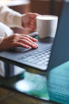 Vertical closeup image of a woman working and touching on laptop computer touchpad while drinking coffee