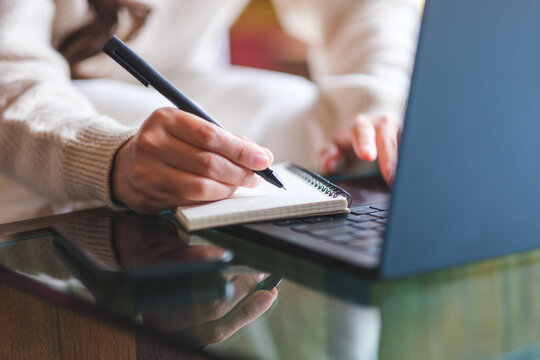 Closeup image of a woman writing on a notebook while working on laptop computer