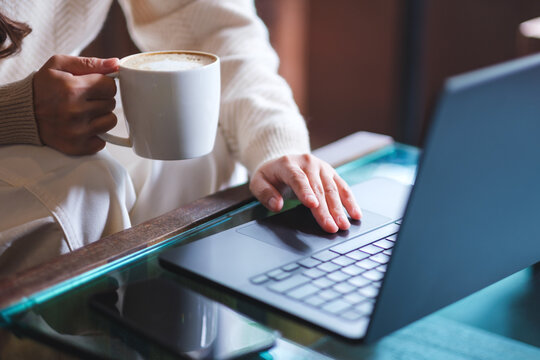 Closeup image of a woman working on laptop computer and drinking coffee in cafe