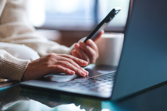 Closeup image of a woman using smart phone and laptop computer in cafe
