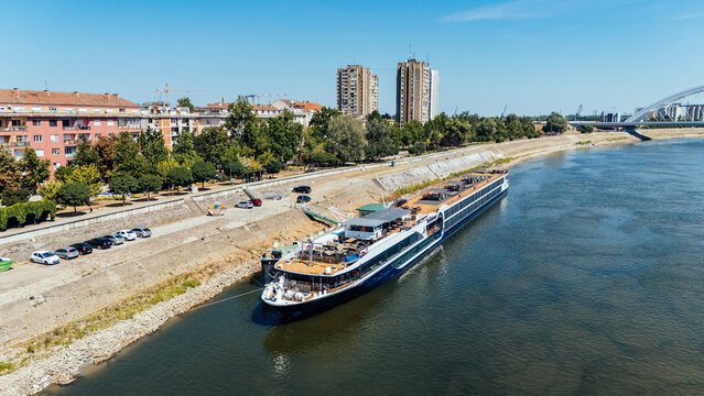 Aerial view of a river cruise ship docked along the Danube river waterfront with the Zezelj Bridge in the background in Novi Sad, Vojvodina, Serbia.