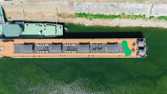 Aerial view of a river cruise ship docked on the Danube river with lounge chairs, tables, and a putting green on the deck in Novi Sad, Vojvodina, Serbia.