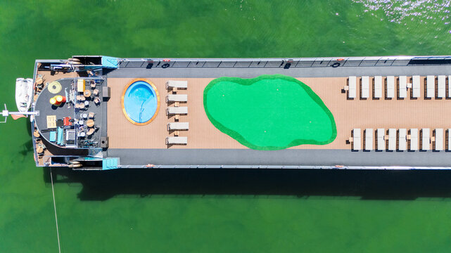 Aerial view of a boat deck featuring a small swimming pool, a putting green, and rows of lounge chairs on the Danube River in Novi Sad, Vojvodina, Serbia.