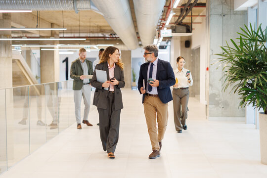 Business colleagues talking while walking in modern office corridor
