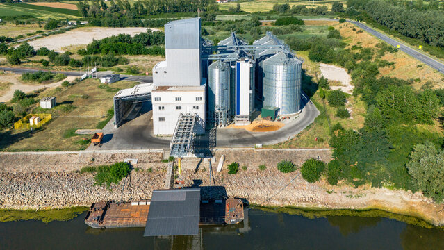 Aerial view of a grain silo facility with metal storage tanks and a conveyor system on the riverbank in Beocin, Vojvodina, Serbia.