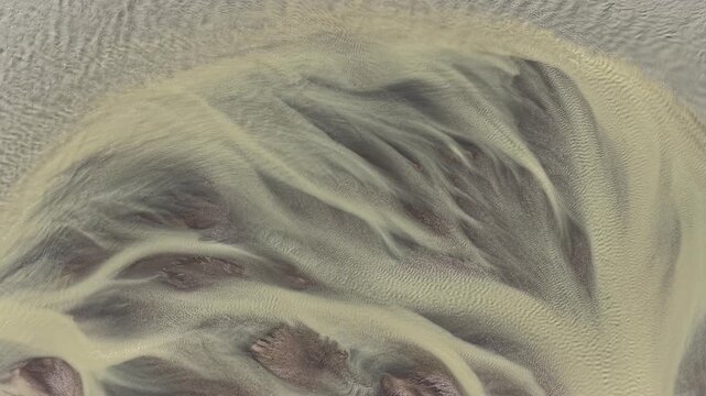 Aerial view of intricate braided glacial river patterns with sediment and sandbars flowing through the landscape of Iceland.