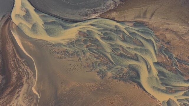 Aerial view of intricate braided river channels and sediment patterns flowing through the volcanic landscape of Iceland.