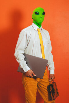 Businessman in an alien mask holds a laptop and briefcase