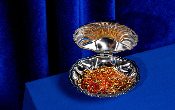 A silver shell contains golden caviar on a blue velvet table