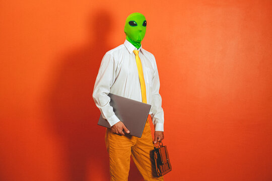 A man in an alien mask holds a laptop in the office