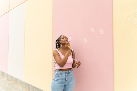 Woman blows soap bubble outdoors against pastel wall