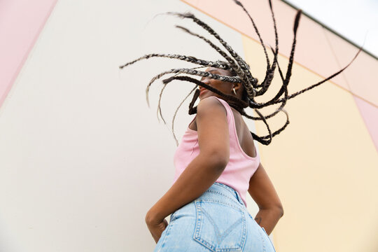Woman swings her braided hair outdoors against a pastel wall