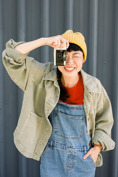 Smiling woman in casual outfit taking photo with analog camera outdoors