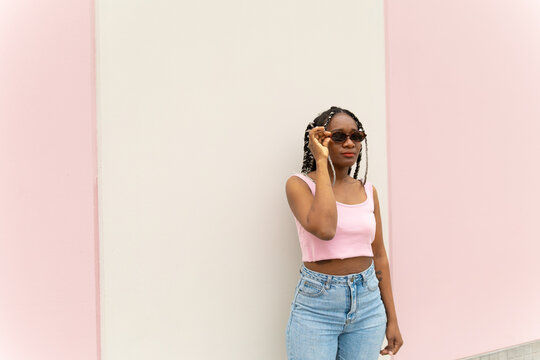 Woman wearing sunglasses poses against a pastel wall