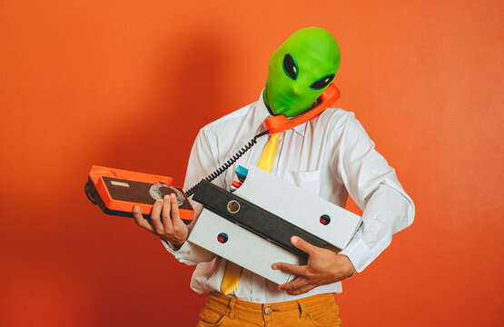 Overwhelmed man in alien mask holding binders and retro telephone