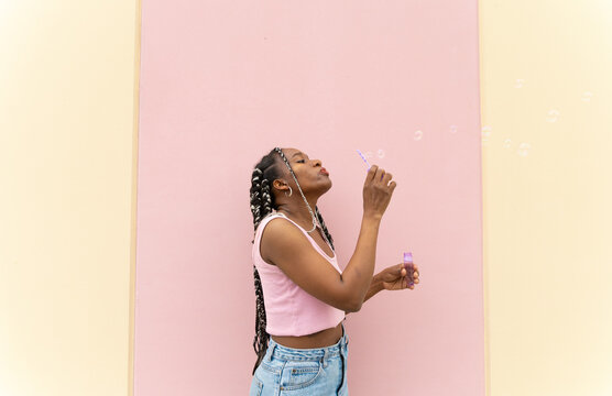 Woman blows a soap bubble against a pastel wall outdoors