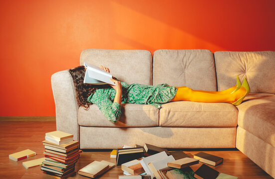 Fatigued woman distracted while reading books on sofa indoors