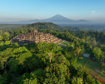 Aerial view of the ancient Borobudur Temple surrounded by lush tropical forests with the majestic Mount Merbabu in the background in Kecamatan Borobudur, Jawa Tengah, Indonesia.