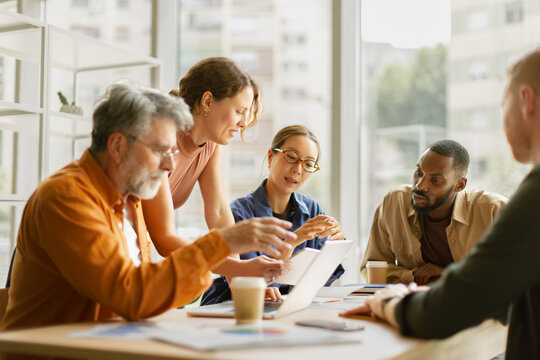 A business team discusses strategy around a laptop in the office