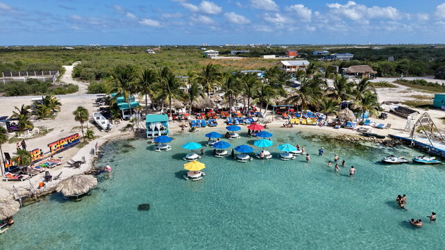 Aerial view of Secret Beach with colorful umbrellas, turquoise water, palm trees, and people swimming in San Pedro, Corozal District, Belize.