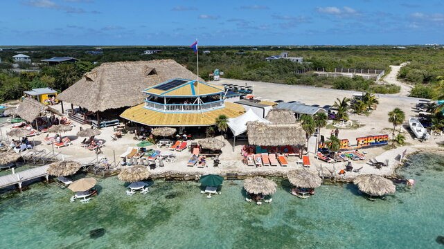Aerial view of a vibrant beach bar with thatched roofs, sun loungers, and turquoise water along the coastline in San Pedro, Corozal District, Belize.