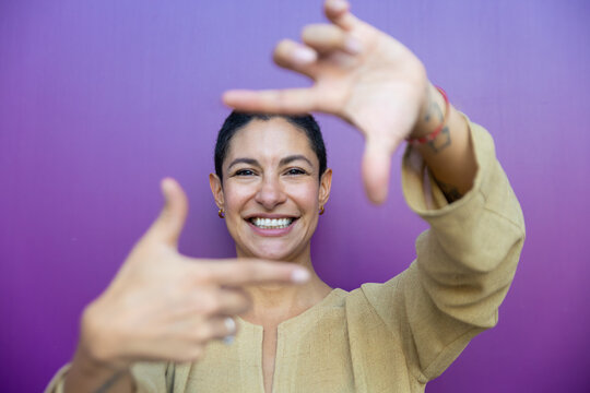 Smiling woman makes hand frame gesture against purple background