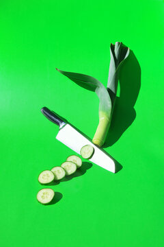 A knife cuts a fresh cucumber and leek on a green background