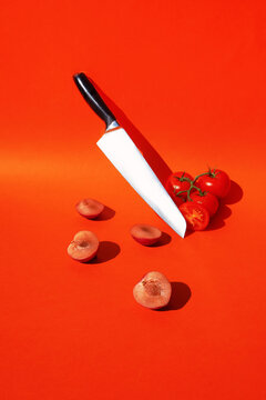 A knife balances between fresh tomatoes and sliced plums on red