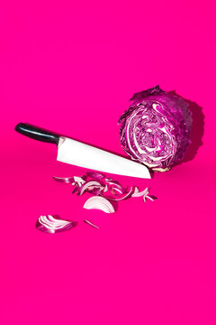 Sliced red cabbage and red onion with knife on pink background