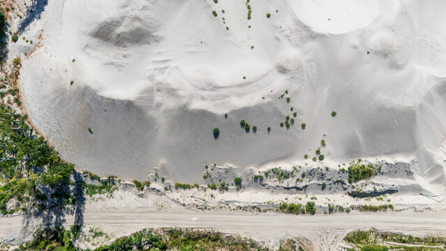 Aerial view of a sand quarry with large white dunes, sparse green vegetation, and a dirt road at the bottom in Novi Sad, Vojvodina, Serbia.