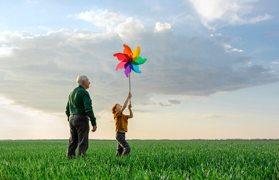 A grandfather and grandson hold a colorful pinwheel in a green field