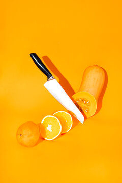 A sharp knife slices an orange and a pumpkin on an orange background