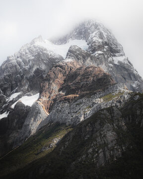 View of Torres del Paine National Park with snow-capped peaks, rugged rock formations, and low-hanging clouds in Chile.