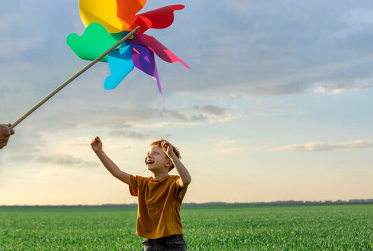 A cheerful boy looks at a colorful pinwheel in a green field