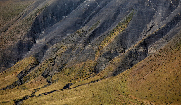 View of the rugged dark rocky slopes and grassy terrain of Torres del Paine National Park in Chile.