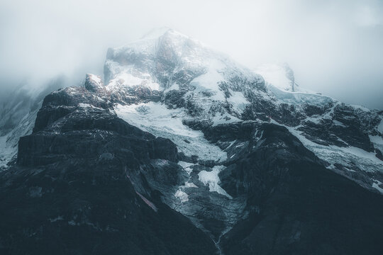 View of Torres del Paine National Park with snow-capped peaks, glaciers, and rocky slopes under a cloudy sky in Chile.